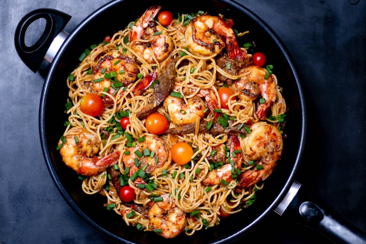 Garlic butter shrimp pasta with linguine, fresh parsley, and lemon wedges in a dark pan