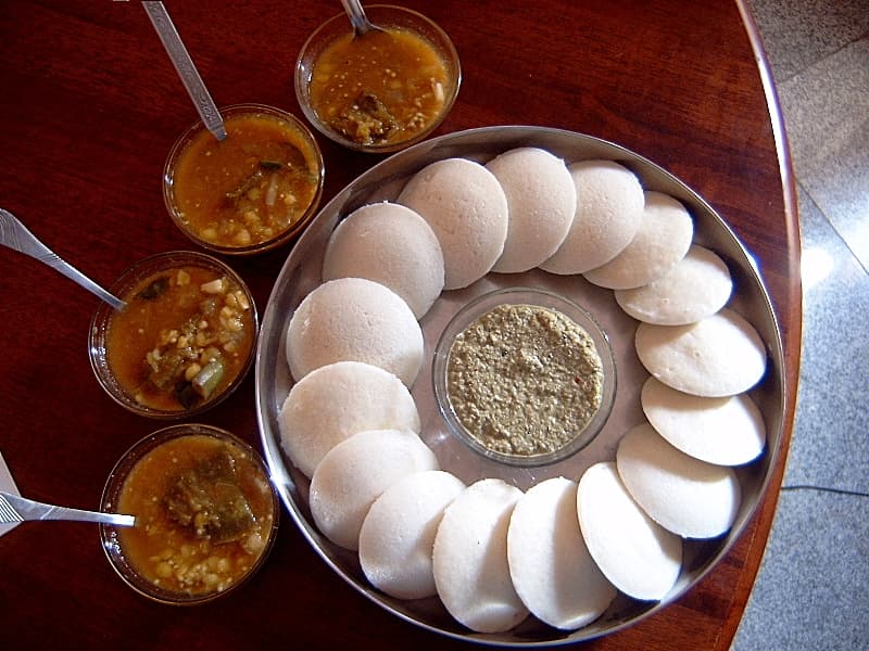 Plate of white idli with bowls of sambar and coconut chutney
