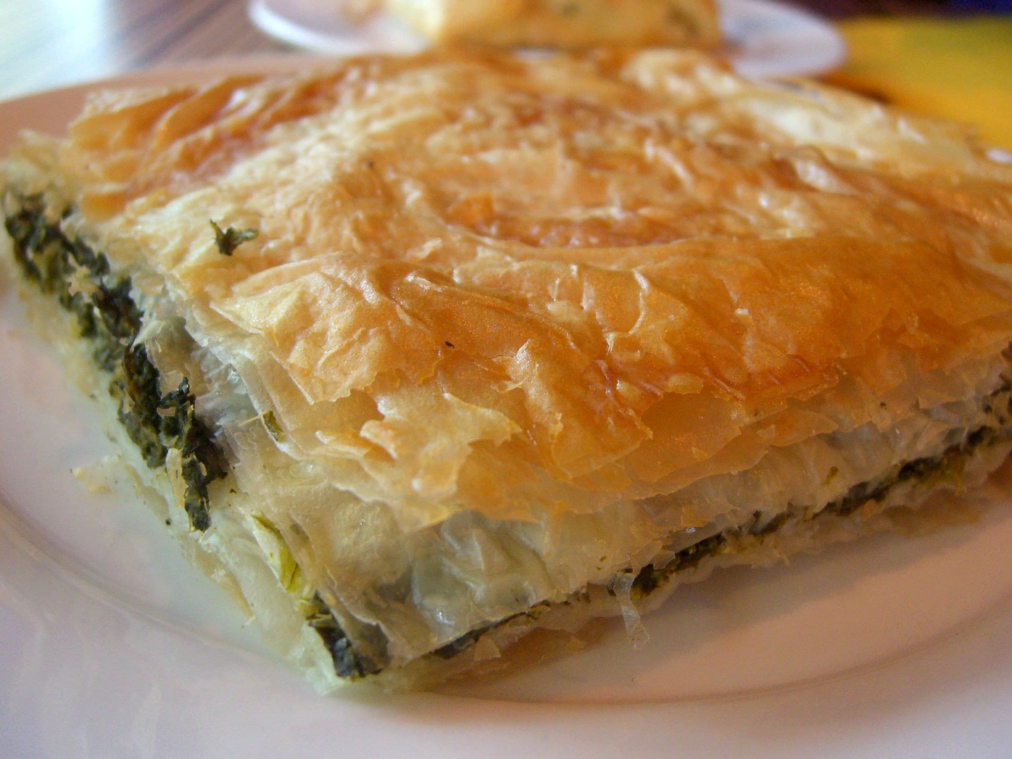 Golden spanakopita cut into squares showing layers of flaky phyllo and green spinach filling