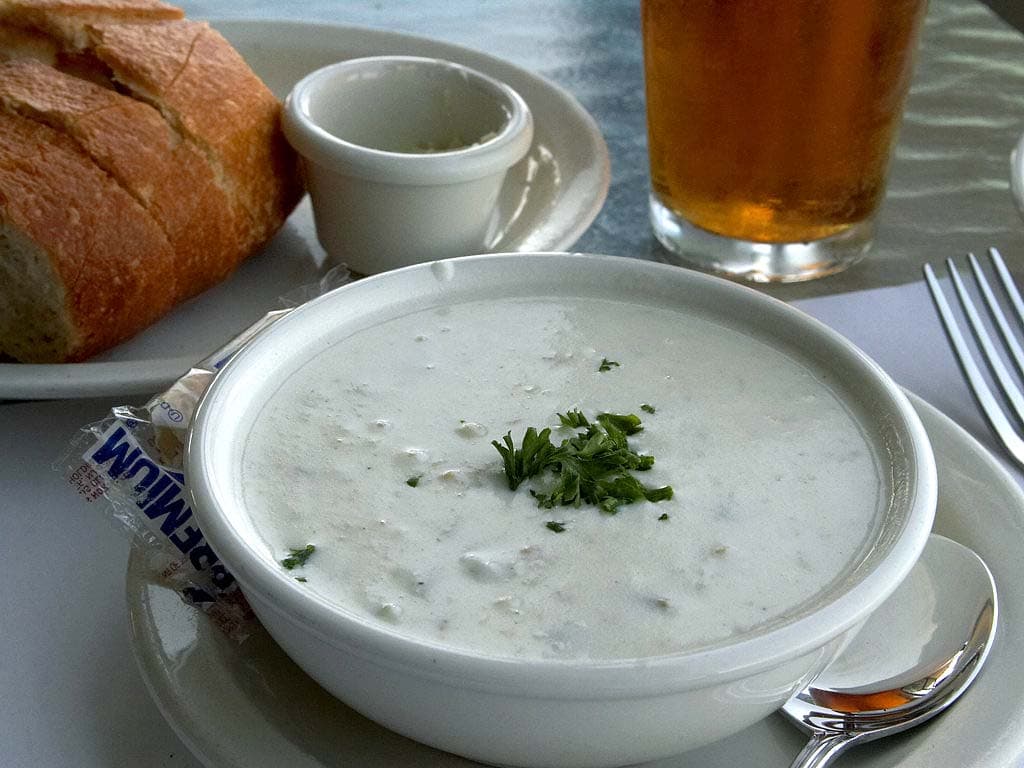 Bowl of creamy New England clam chowder topped with crackers and fresh chives