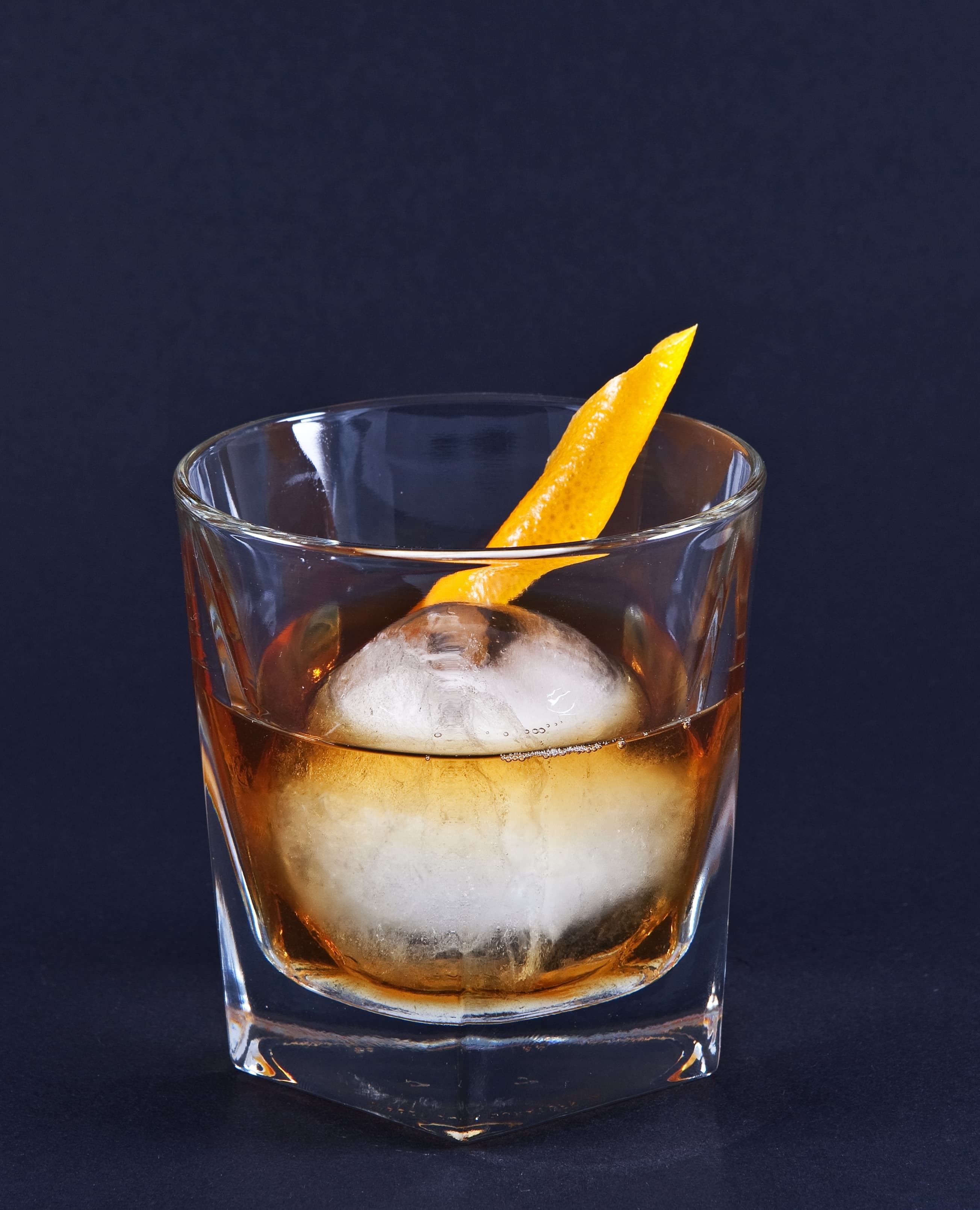 Old fashioned cocktail with large ice cube and orange peel