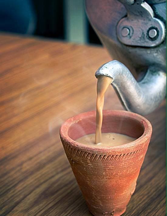 Masala chai in a glass cup with whole spices beside it