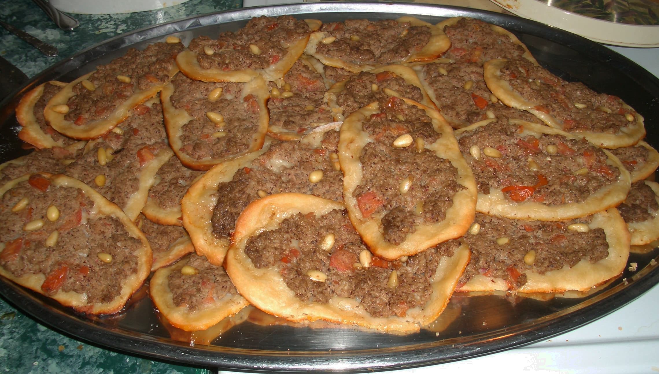 Tray of golden sfiha Lebanese meat pies with lemon wedges