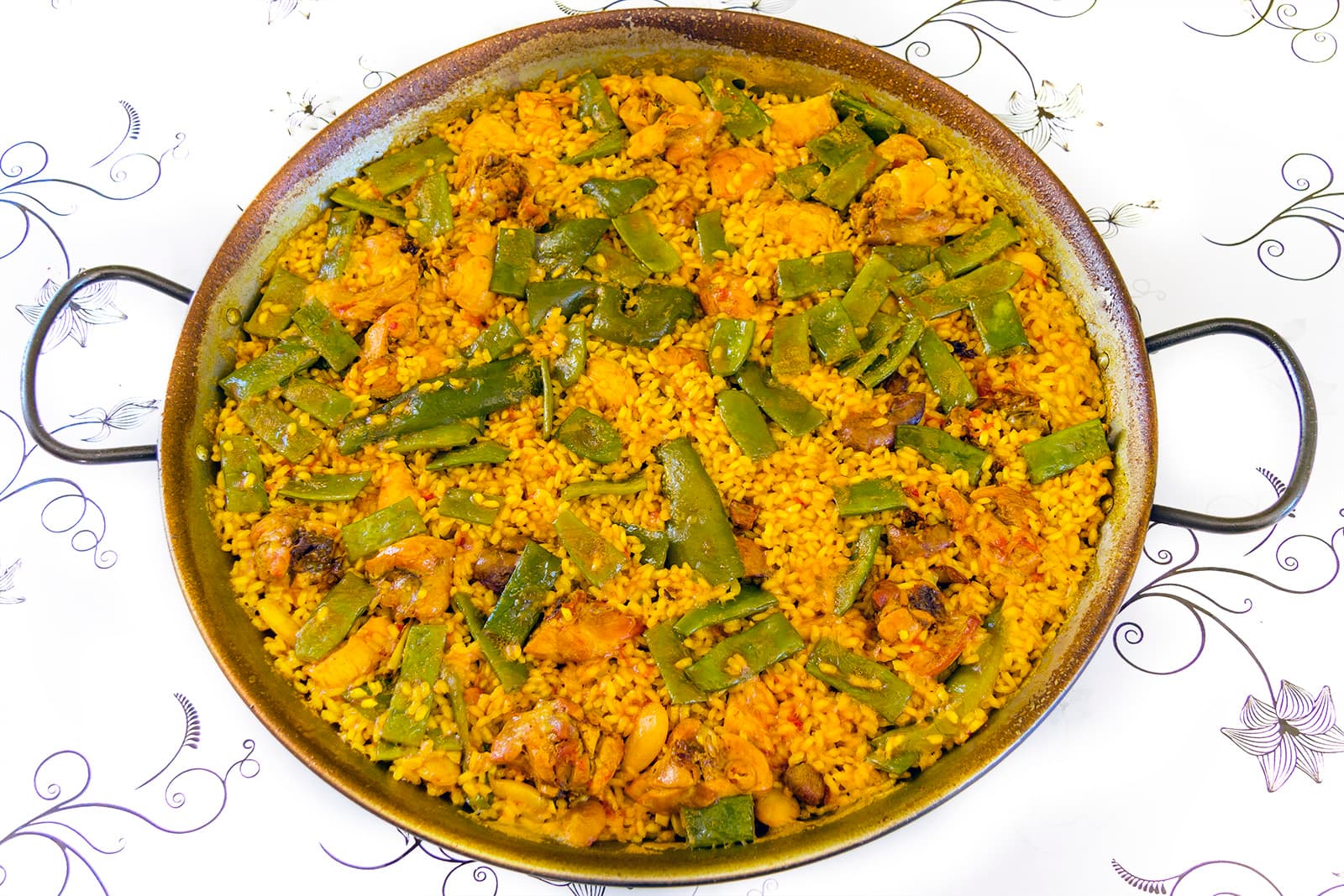 Colorful vegetable paella with saffron rice in a traditional paella pan