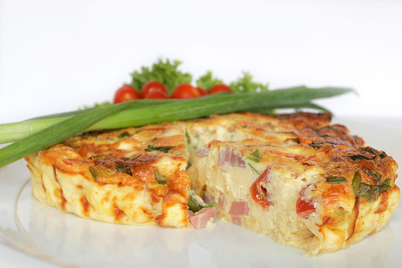 Golden vegetable frittata in a cast iron skillet with visible vegetables and herbs