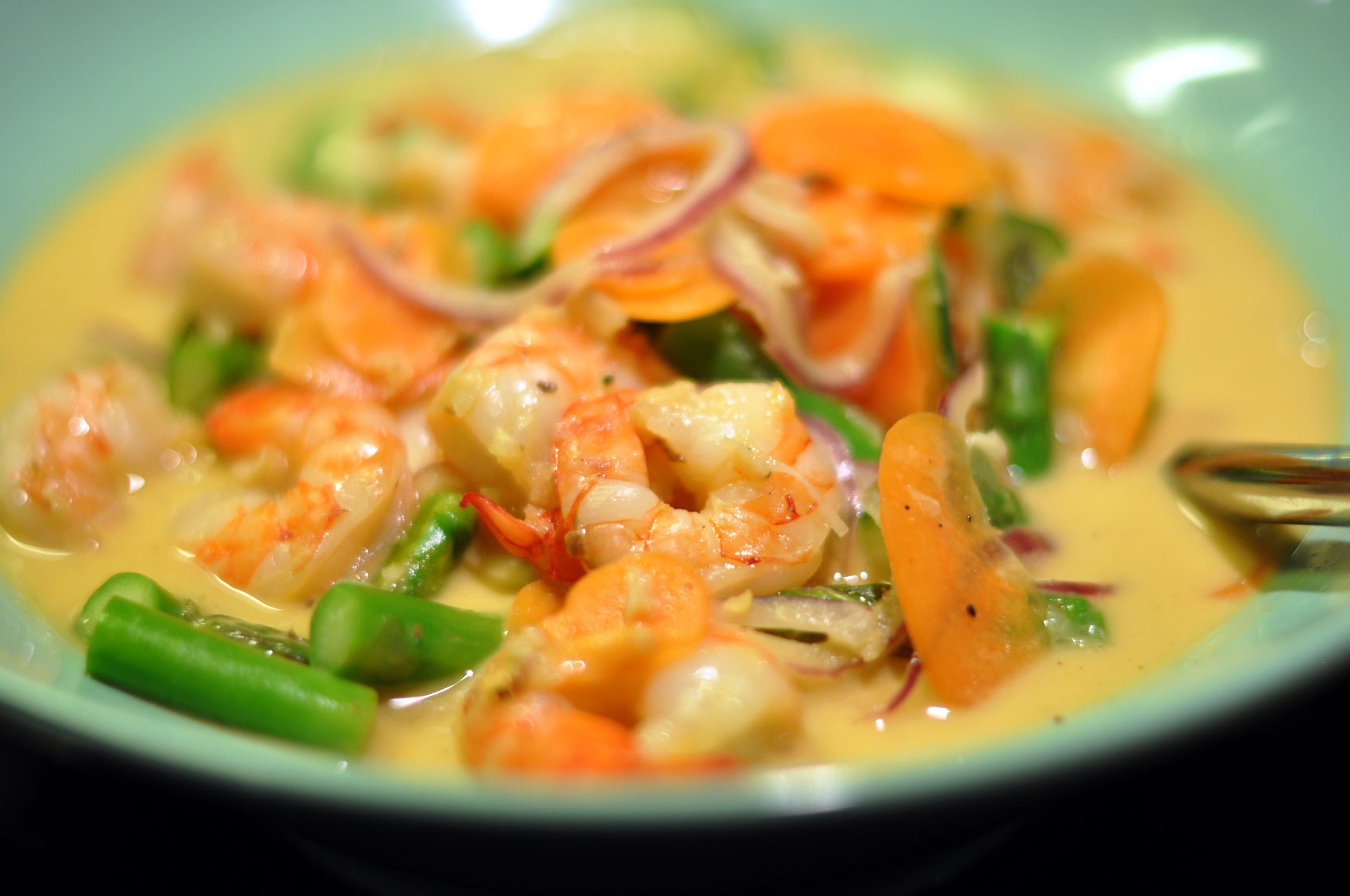 Creamy prawn malai curry in a white bowl with green chilies